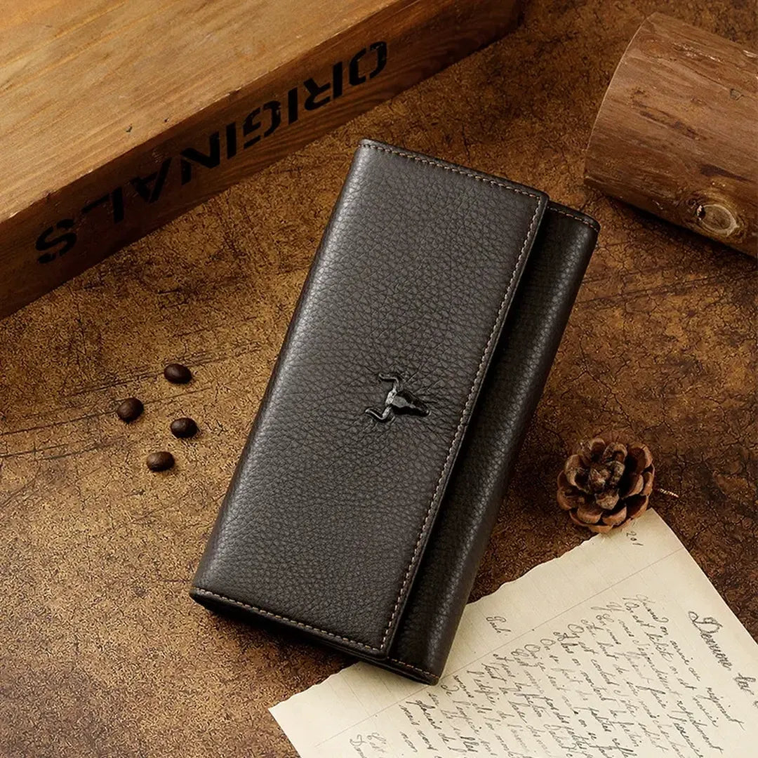 MING CLAN Men's Long Trifold Brown Leather Wallet displayed closed on a rustic wooden desk